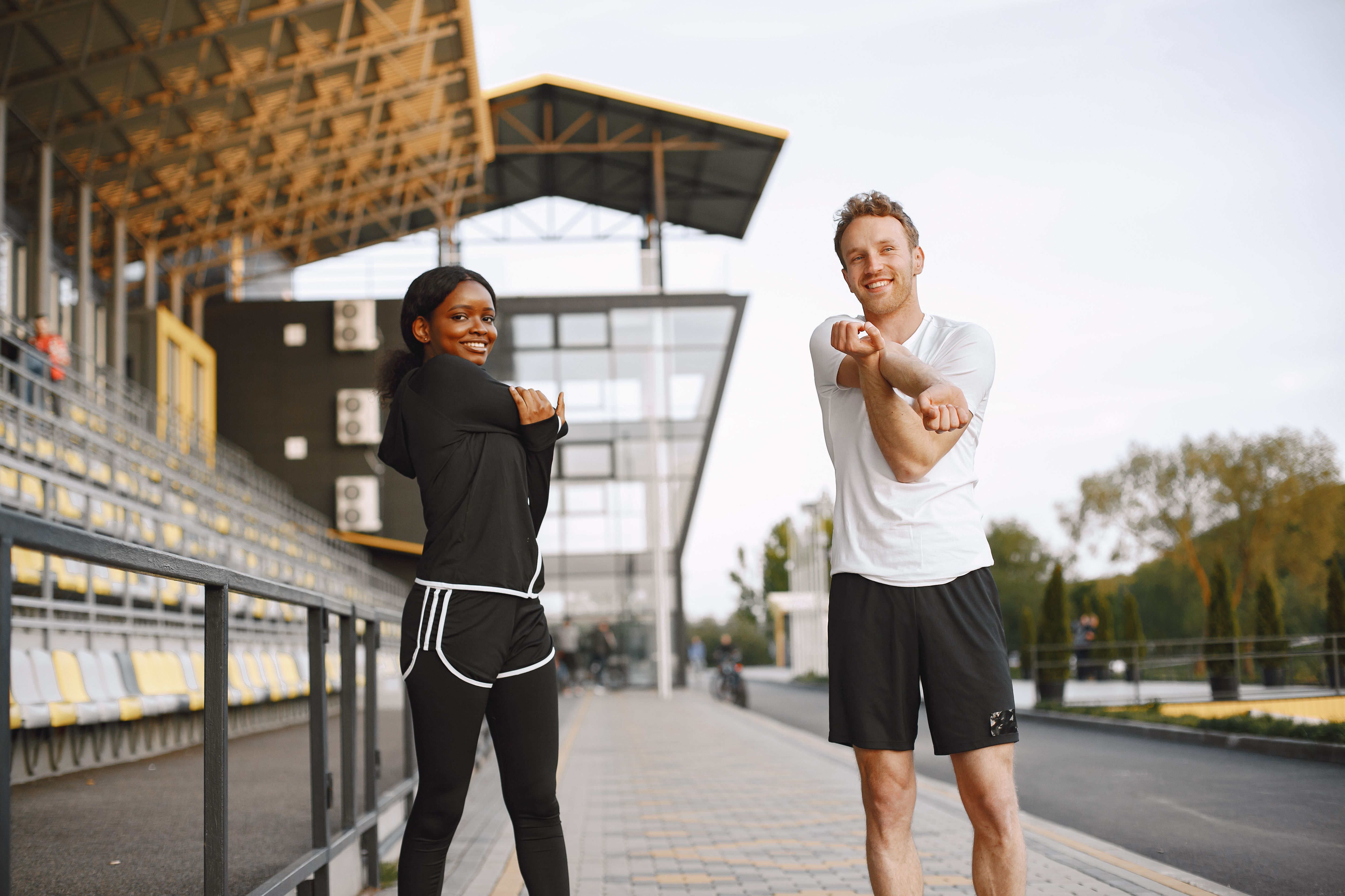 Two friends stretching together at an outdoor stadium