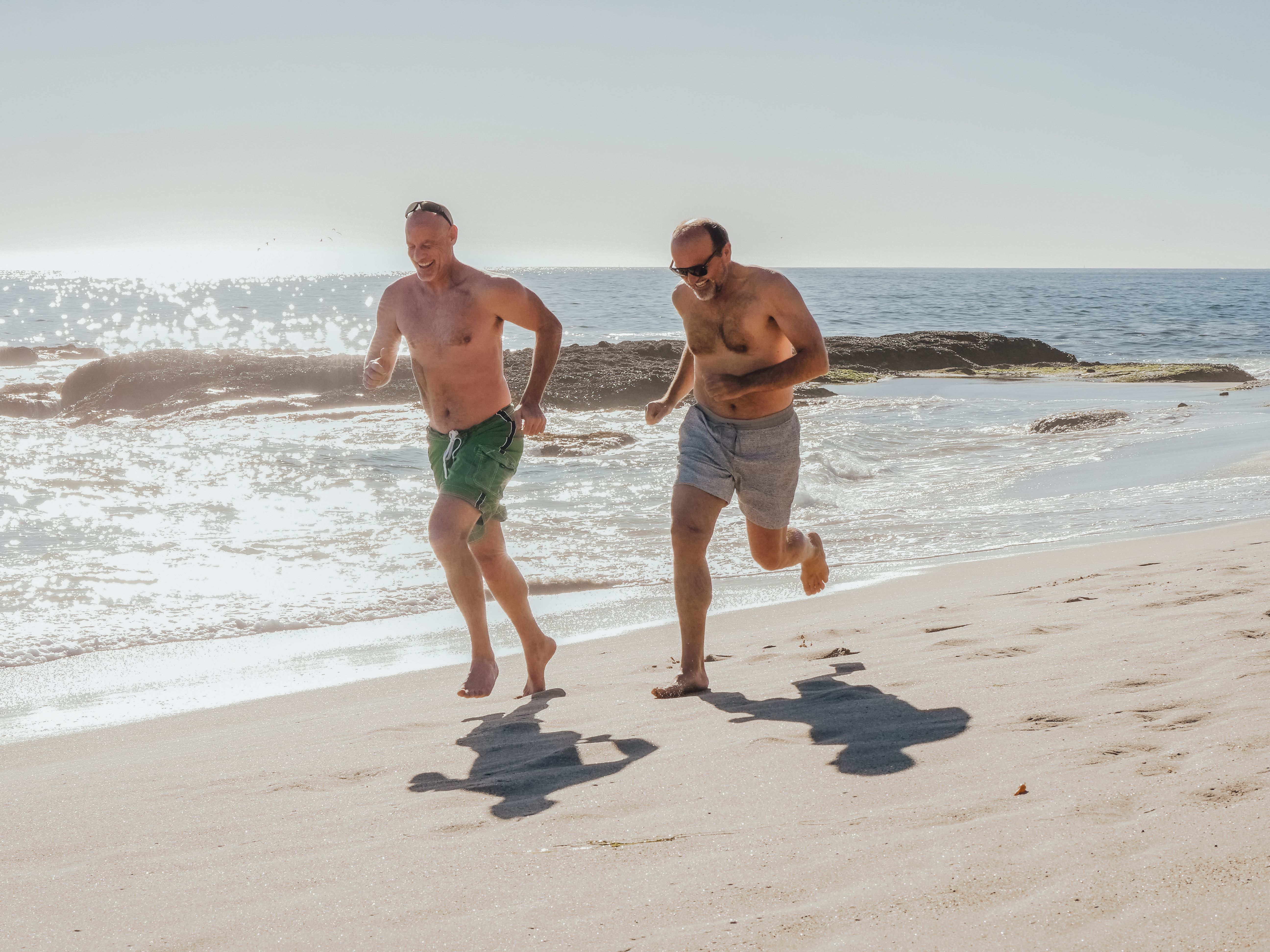 Two men laughing as they run together along a beach