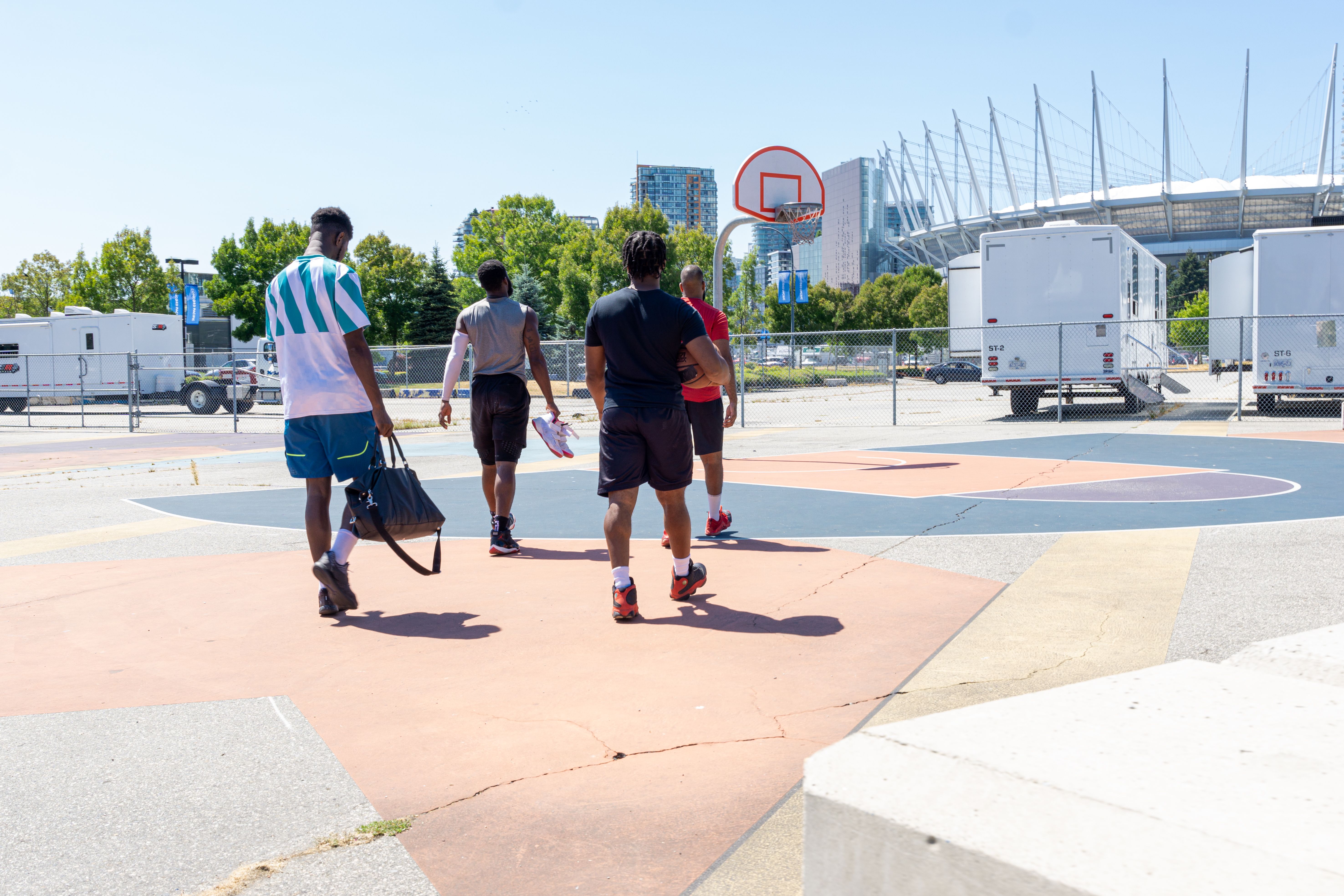 Four friends walking towards an outdoor basketball court in sunshine